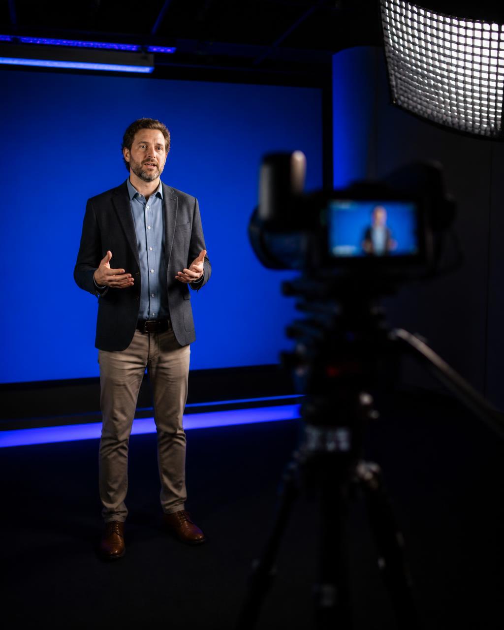 Docente che registra una videolezione davanti a un blue screen in uno studio tecnologico